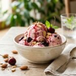 Creamy almond cherry Italian ice cream scooped in a ceramic bowl with Amarena cherries and toasted almond slivers